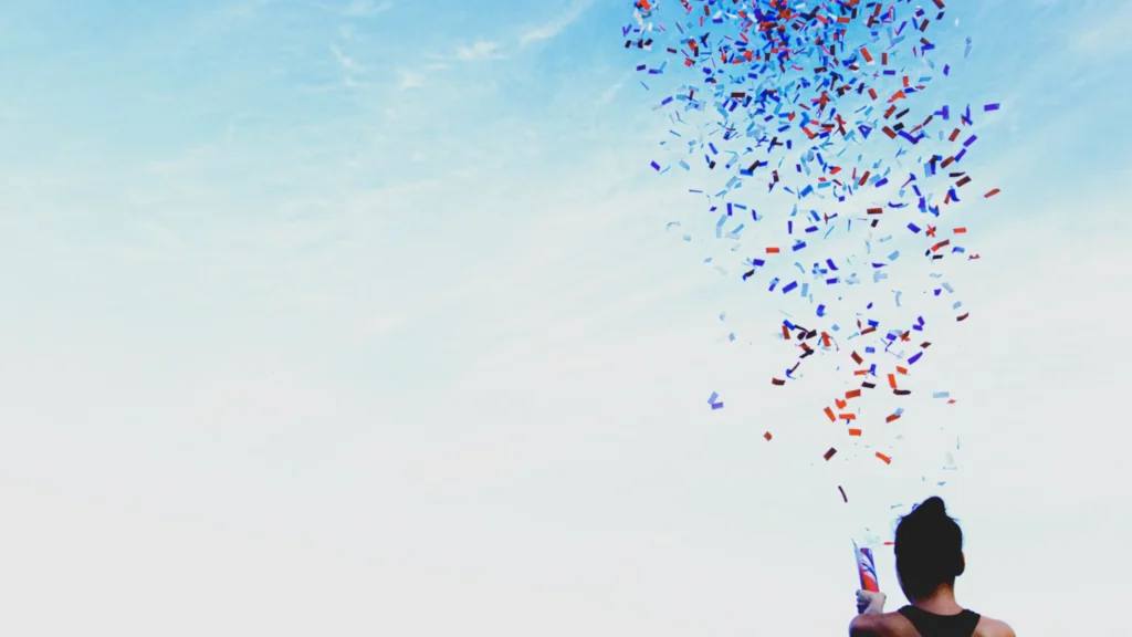Erfolge feiern – eine junge Frau jubelt über erreichte Ziele mit einer Konfettikanone